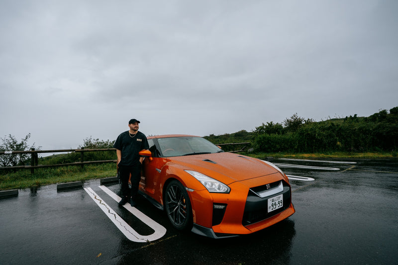 Client leaning on an orange GT-R at a rainy Hakone viewpoint
