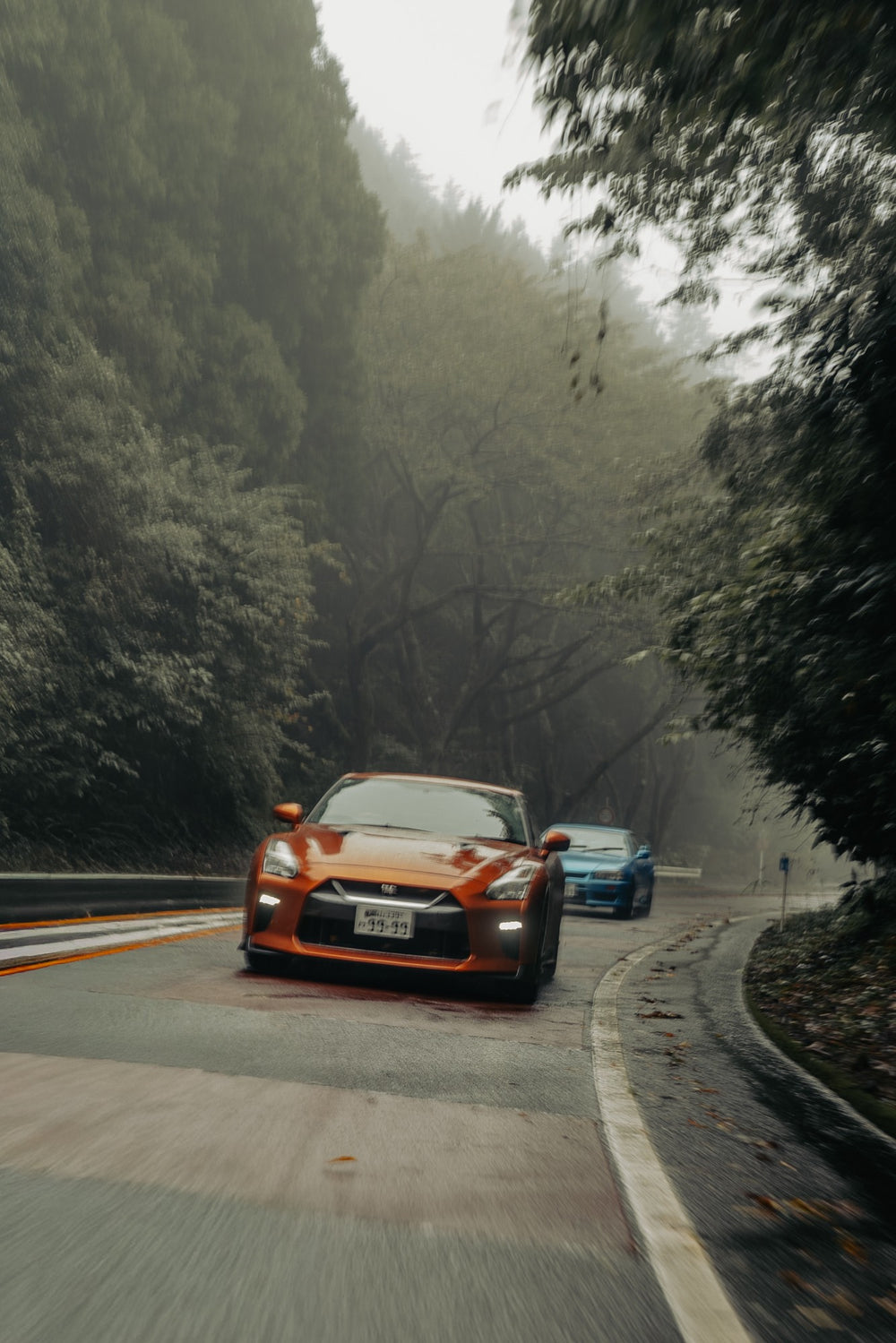 Orange GT-R and blue Skyline R34 on a misty Hakone mountain road